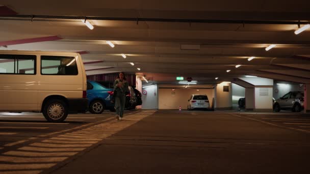 走在地下停车场的妇女 妇女沿着停放的汽车在地下停车场散步 — 图库视频影像