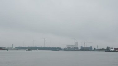 Antwerp Limanı. Antwerpen limanında rüzgar türbinleri. Beyaz rüzgar türbinleri sisli gri gökyüzünde dönüyor. Yeşil enerji üretiyorlar. Yenilenebilir kaynaklar çevre elektrik gücü