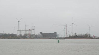 Antwerp, Belçika 'da endüstri. Arka planda Antwerp şehrinin sanayi bölgesinde dönen beyaz bıçaklı yel değirmenleri. Alternatif yeşil enerji üretimi. Antwerp Limanı Sisli bir günde