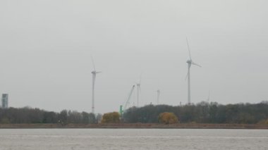 Belçika, Antwerp 'te dönen rüzgar türbini pervaneleri ve sanayi bölgesi. Rüzgâr türbinleri sisli gri gökyüzüne karşı dönüyor. Alternatif yeşil enerji üretiyor. Yenilenebilir kaynaklar çevre gücü