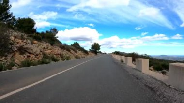 Man climbing on bicycle along mountain asphalt road against blue sky and clouds. Cyclist riding on bike in mountains. Road biker cycling uphill through mountain. Sport concept. Active lifestyle