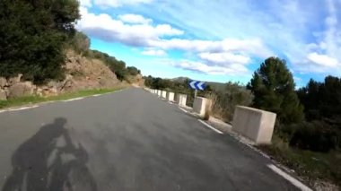 Tepe dağ yolundan hızla inen bisikletçinin silueti. Dağ geçidinden bisiklete binen profesyonel bir bisikletçi. Adam boş asfalt yolda iniyor. Bisiklet konsepti. Spor etkinliği