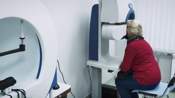 現代の機器の助けを借りて視力検査を行う眼科キャビネットの椅子に座っているシニア女性 女性の年金受給者は光学機器で視力をチェックします 眼科治療 — ストック動画