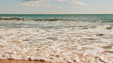 Sea waves crashing on sandy beach and creating white foam. Seashore of Mediterranean Sea at sunny day. Seascape with clear sea water. Amazing nature landscape