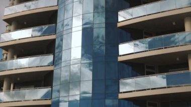 Skyscraper with sky and clouds reflections on glass surface. Business offices. High modern glass building with reflection of fast moving white fluffy clouds against blue sky