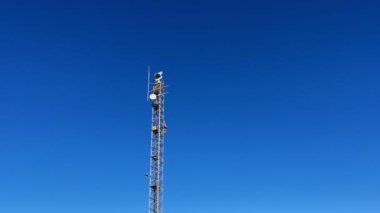 Radar tower station with spinning antennas and surveillance camera against clear blue sky. Coastal industrial military radar transmitting and receiving signals