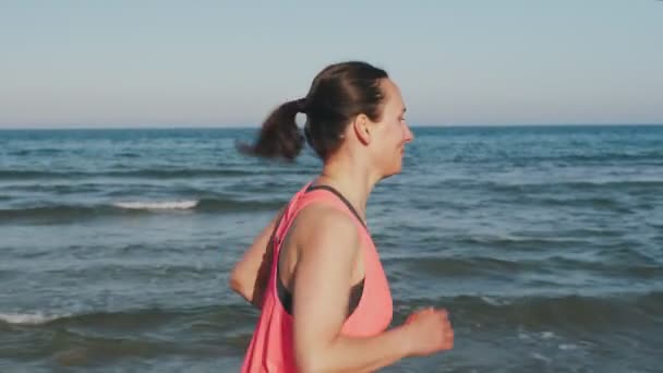 毎日のルーチンの一環として 午前中にビーチに沿って実行している若い女性の動機付け 自信のある女性ランナーのトレーニングを屋外にフィット 海辺でスポーツ活動中の女の子ジョギング 心臓フィットネス演習を行う — ストック動画