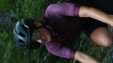 Şık bisiklet gözlüklü, formda bir kadın bisiklet sürüyor. Dikey video. Bisiklet üzerinde profesyonel kadın bisikletçi eğitimi. Ormanda bisiklete binen bir sporcu. Triatlon konsepti. Spor etkinliği