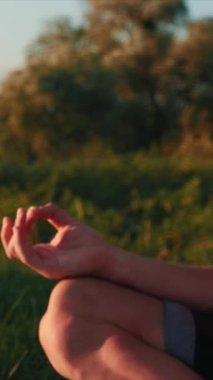 Parkta yeşil çimlere karşı erkek yüzü. Dikey video. Yoga yapan, meditasyon yapan ve rahatlatan bir adam. Yoga sporcusu erkek yeşil çimlerde yoga halısında oturuyor ve temiz havanın tadını çıkarıyor.