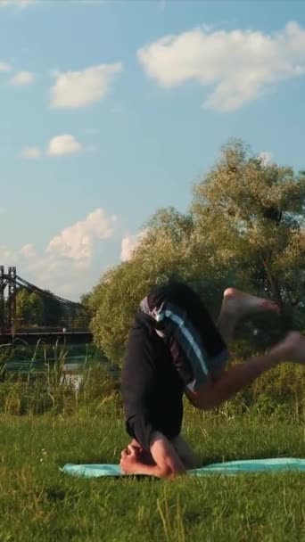 手を取り合ってる 公園のヨガマットの上で上下にバランスをとるアスリート男性 垂直ビデオ 屋外でバランスポジションを練習する人 フィットネス活動 ヨガの練習 セルフケアルーティン — ストック動画