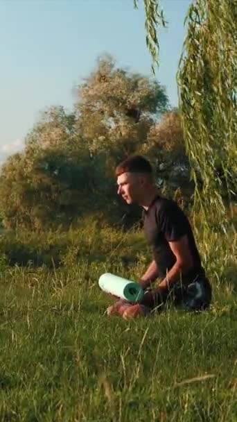 ヨガの瞑想を練習する男 垂直ビデオ 魅力的な選手の男性は自然の中で瞑想 ヨガの男は ヨガの瞑想の練習中に緑の公園で新鮮な空気をリラックスして楽しむ — ストック動画