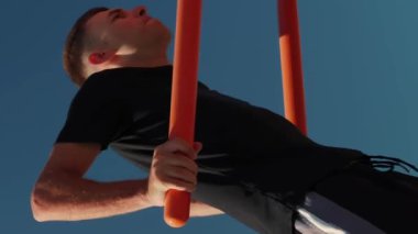Spor giyimli genç bir adam spor sahasında antrenman yapıyor. Dikey video. Erkek sporcu barlara yanaşıyor. Erkek, fitness egzersizi yapıyor. Adam dışarıda antrenman yapıyor. Spor konsepti