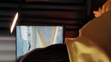 Kulaklıklı genç kız çevrimiçi bilgisayar oyunu oynuyor. Dikey video. Sanal oyuncular evdeki bilgisayarda oyun oynuyorlar. Oyuncu yaşam tarzı. E-Spor çevrimiçi oyun teknolojisi