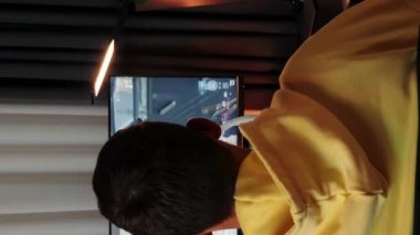 Erkek oyuncunun evde masa masa oynadığı arka plan görüntüsü. Dikey video. Profesyonel siber oyuncu kablosuz kulaklık takar ve online video oyunu oynamaya başlar. E-spor ve çevrimiçi oyunlar