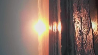 Deniz suyunun üzerinde altın pembe günbatımı. Deniz ufkunda batan renkli gökyüzünde güneş. Deniz dalgaları sahile çarpıyor. Dikey video. Akşam karanlığında güzel deniz manzarası