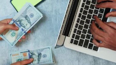 Ofis masasında para sayan biri. Dikey video. Ortaklar çalışma masasında anlaşırlar, dizüstü bilgisayarda yazı yazarlar ve kağıt para sayarlar. İş konsepti