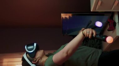 Evde video oyunu oynayan ve video kulaklık kullanan genç bir kız. Dikey video. VR gözlük takan neşeli bir kadın, online video oyunları oynuyor. Sanal gerçeklik, yenilik ve teknoloji. Oyun konsepti