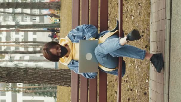 女生在户外学习 在公园工作的自由职业者 垂直录像 在城市公园的笔记本电脑上工作的女自由撰稿人戴着防护面具 大自然的自由职业者 — 图库视频影像