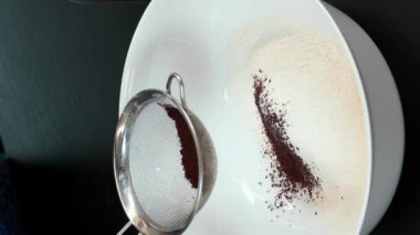 Kakao tozunu un ile süzgeçten geçirip kaseye koymak. Dikey video. Modern mutfakta çikolatalı bisküvi hazırlayan kadın. Kadın pastacı evde tatlı kurabiyeler pişiriyor. Ev yapımı hamur işleri