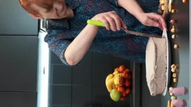 Kadın pastacı spatula kullanarak kremayla pasta dekore ediyor. Dikey video. Kadın ev yapımı tatlı kek pişiriyor, pastayı kremayla süslüyor. Evde pişirme ve pişirme.