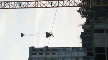 Mavi gökyüzüne karşı inşaat alanında çalışan yüksek kule vinci. Dikey video. İnşaat alanında konut inşaatı için malzeme taşıyan bir vinç. İnşaat ve inşaat endüstrisi
