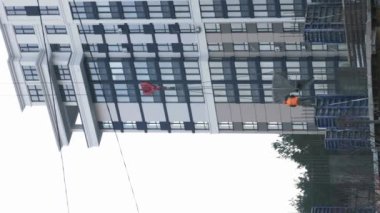 İnşaat vinci ve inşaat alanında çalışan işçiler. Dikey video. İnşaat alanında vinç yükleme ve inşaat malzemeleri taşıma. Modern cam konut kompleksi.