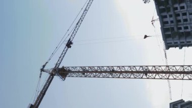 İnşaat alanında yüksek kule vinci. İnşaatta çalışan işçiler. Dikey video. Yeşil şehir bölgesinde modern cam konutların inşaatı. İnşaat ve emlak endüstrisi