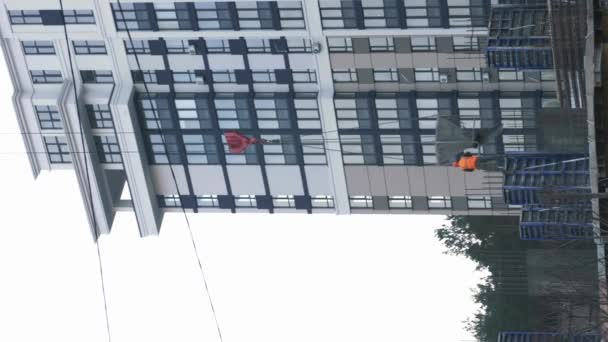 建設クレーンや建設現場で働く労働者 垂直ビデオ タワークレーン建設現場で建築材料をロードし 現代的なガラス住宅団地の建物 — ストック動画