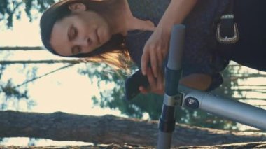 Şehir parkında gün batımında elektrikli scooter kiralayan bir kadın. Dikey video. Elektrikli şehir scooter 'ı kiralamak için akıllı telefondan gülümseyen genç kadının portresi