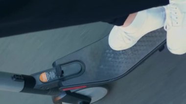 Şehir parkında elektrikli scooter kullanan birine yakın çekim. Dikey video. Scooter tekerleği dönüyor, asfalt yolda gidiyor. Kişisel ekolojik şehir ulaşımı. E-scooter kullanan kadın.