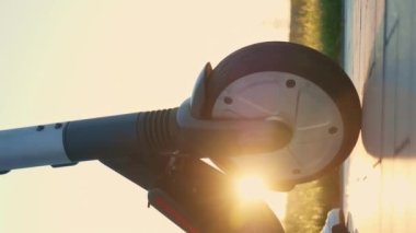 Gün batımında e-scooter, yakın çekim. Dikey video. Akşam karanlığında elektrikli scooter sürmeye başlayan biri. Park etmek için şehir scooter 'ı kiralayan bir turist. Ekoloji kişisel taşımacılığı