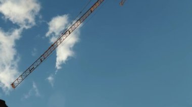 Yüksek kule vinci mavi gökyüzüne karşı kabarık bulutlar. Dikey video. İnşaat vinci inşaat alanında çalışıyor
