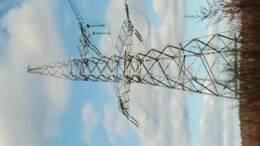 Elektrik yüksek voltaj iletim kulesi devrede, zaman aşımı. Dikey video. Mavi gökyüzü ve bulutlara karşı kablolu ve kablolu elektrik direği