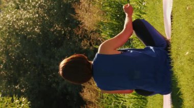 Spor salonundaki kadın güneş doğarken göl kenarında yoga yapıyor. Spor yapan atletik kadın sabah doğasında vücut esneme egzersizi yapıyor. Dikey video. Gün batımında yoga. Nehir kenarında meditasyon yapan kadın.