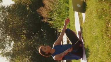 Doğada laptopla yoga yapan bir kadın, online dersler alıyor. Dikey video. Yoga minderinde oturup nehir kenarında meditasyon yapan genç bir kadın. İnternetten yoga dersleri izliyor.