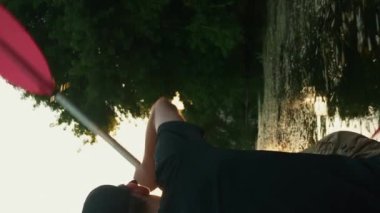 Aktif genç adam gün batımında kanoda kürek çekiyor. Dikey video. Atletik erkek sporcu yaz akşamı kano yapıyor. Açık hava eğlence aktivitesi. Boş zaman aktivitesi. Aktif sağlıklı spor yaşam tarzı