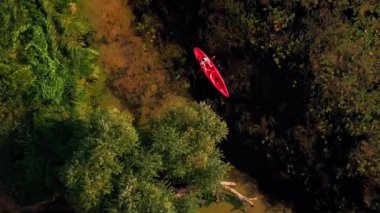 Gün batımında kayak yapan birinin havadan görünüşü. Su sporu aktivitesi. Dikey video. Aktif bir kadın, altın gün batımı ışıklarıyla kırmızı kanoda kürek çekiyor. Kadın hafta sonunu dışarıda geçiriyor.