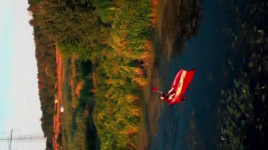 Yazın nehirde kayak yapan biri. Aktif insanlar. Dikey video. Turist, altın gün batımı ışıklarıyla kanoyla su üzerinde kürek çekiyor. Spor aktivitesi. Boş zaman aktivitesi