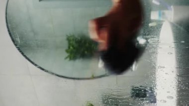 Duşluk cam temizleyici ve mendille duş camı temizleyen kadın. Dikey video. Kadın süngerle duş camı temizliyor.