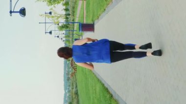 Şehir parkında yaya yolu boyunca koşan kadın sporcu. Dikey video. Spor giyimli atletik bir kadın dışarıda koşuyor, sağlıklı yaşam tarzını sürdürüyor. Spor aktivitesi. Spor egzersizleri.