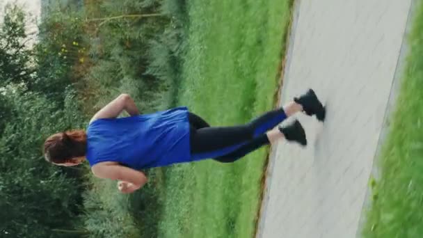 緑の都市公園を走る若いスポーツ女性 垂直ビデオ フィットネスカーディオ活動を屋外で行う女性ランナーは アクティブな健康的なライフスタイルを維持します 激しいワークアウト演習 — ストック動画