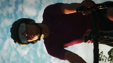 Gün batımında dışarıda bisiklet süren bir kadın. Dikey konsept. Profesyonel yol bisikletçisi şık bisiklet kaskı ve gözlüklü bisiklet eğitimi alıyor, kardiyo fitness egzersizleri yapıyor. Etkin yaşam biçimi