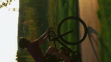 Akşamüstü gün batımında bisiklet süren bisikletçi silueti. Dikey video. Günbatımında bisiklet süren profesyonel bir bisikletçi. Kadın dışarıda bisiklet sürüyor, kardiyo fitness egzersizleri yapıyor. Spor egzersizi.