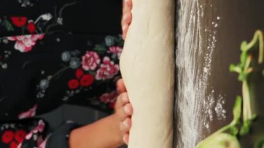 Koyu ahşap masada ev yapımı pizza hamuru yoğuran kadın şef. Dikey video. İtalyan pizzasını evde hazırlayan kadın. Lezzetli sağlıklı yiyecekler yapma süreci