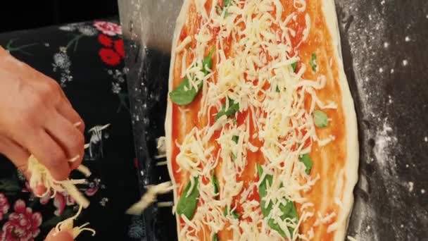 ピザにすりおろしたチーズを広げる手 垂直ビデオ 家庭でピザを調理する イタリアの自家製ピザを作る女性 新鮮な生地にチーズを追加 おいしい健康食品を作るプロセス — ストック動画