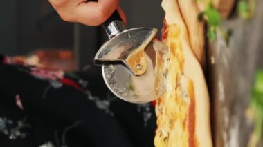 Pizza bıçağıyla pizzayı dilimleyen kişi, yakın plan. Dikey video. Kadın eli hazırlanmış ev yapımı pizzayı parçalara ayırıyor. Mutfak konsepti
