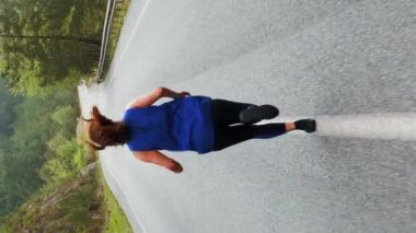 Yağmurlu bir sabahta dağda koşan bir kadın. Dikey video. Spor eğitimi. Kilo vermeye çalışan tombul bir kadın ormanda asfalt yolda koşuyor. Spor motivasyonu