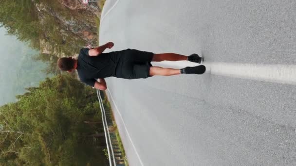 屋外で走っている男 バーティカルビデオ スポーツトレーニング 山の空のアスファルト道路でスポーティブなアスレチック男性ジョギング 森で激しい心臓運動を行い 健康的なライフスタイルを維持 — ストック動画