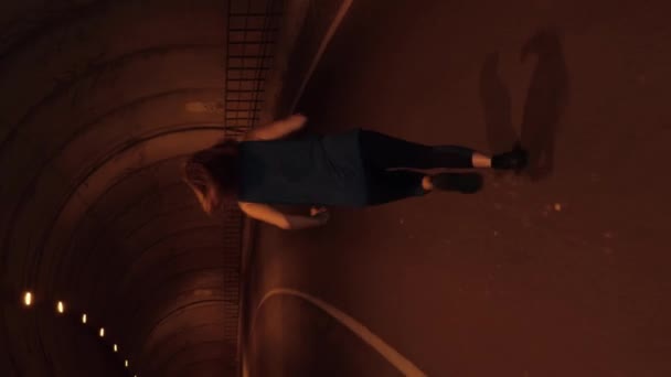 女人在黑暗的隧道里奔跑女性穿着运动服在空旷的柏油路上通过隧道在夜间慢跑 体育培训 垂直录像 做高强度有氧运动的运动员 — 图库视频影像