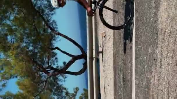 骑自行车的职业训练 骑自行车活动 垂直录像 身穿白色头盔和鞋子的年轻健康男子骑公路自行车与海风相映成趣 男性积极参加健身活动 — 图库视频影像